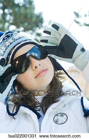 Stock Image - Teenage girl wearing winter clothes, adjusting sunglasses, portrait. Fotosearch