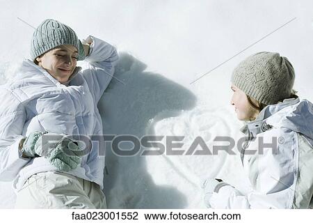 Stock Image - Teenage girls lying on snow, heart with initials drawn on surface of snow. Fotosearch