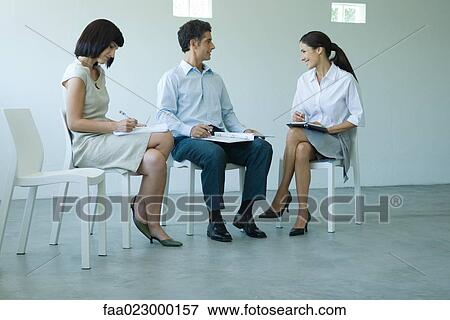 Stock Photo - Three business associates sitting on chairs, holding documents on laps, talking. Fotosearch