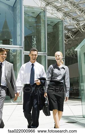 Stock Photograph - Three business associates walking together, all smiling, two looking at camera. Fotosearch