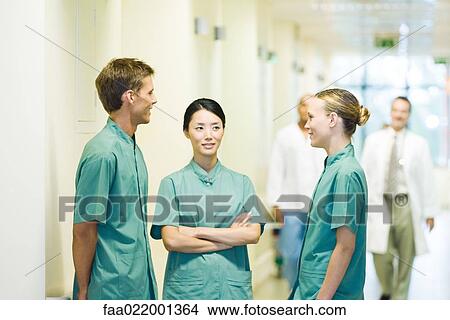 Picture - Three medical workers chatting in hospital corridor. Fotosearch