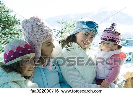Stock Photograph - Three teen or preteen girls with toddler in mountains, all wearing winter coats and hats, portrait. Fotosearch