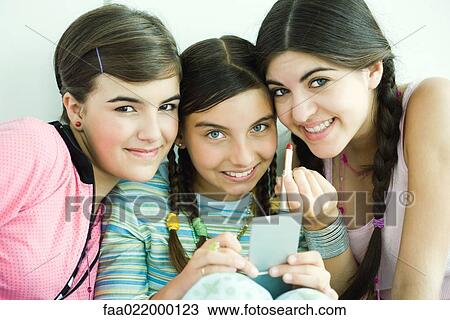 Stock Image - Three young female friends holding make-up, smiling at camera. Fotosearch