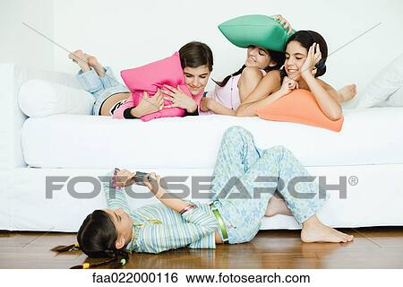 Three young female friends lying down, holding cushions while fourth friend takes photo View Large Photo Image Stock Photograph - Three young female friends lying down, holding cushions while fourth friend takes photo. Fotosearch
