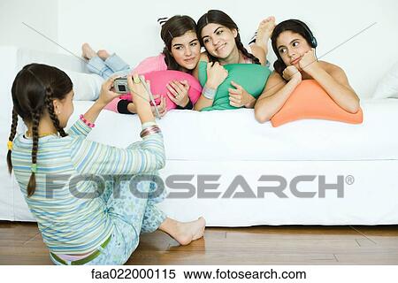Stock Photography - Three young female friends lying with heads on cushions while fourth friend takes photo. Fotosearch
