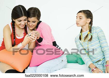 Three young female friends sitting on sofa, two looking at cell phone together while third watches View Large Photo Image Stock Photo - Three young female friends sitting on sofa, two looking at cell phone together while third watches. Fotosearch
