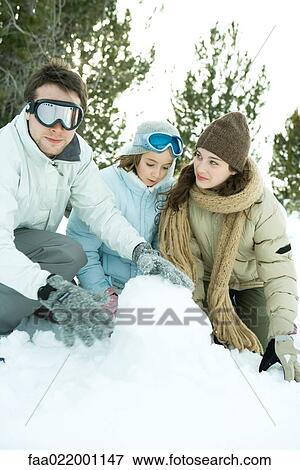 Stock Photo - Three young friends crouching in snow, making snowball, one looking at camera. Fotosearch