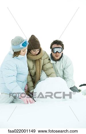 Stock Photo - Three young friends crouching in snow, making snowball, one looking at camera. Fotosearch