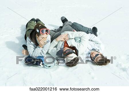 Stock Photograph - Three young friends reclining in snow, one holding head. Fotosearch