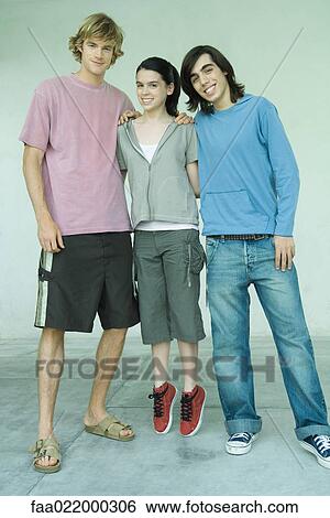 Three young friends, teen girl standing on tiptoes between two male friends, full length portrait View Large Photo Image Stock Photograph - Three young friends, teen girl standing on tiptoes between two male friends, full length portrait. Fotosearch