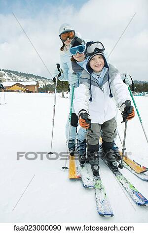 Stock Image - Three young skiers standing together, lined up, smiling at camera. Fotosearch