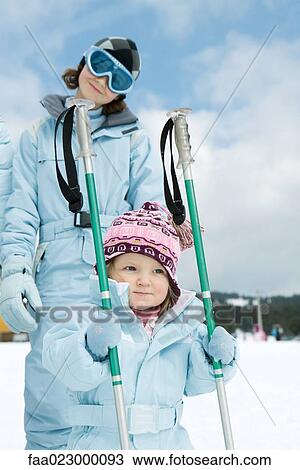 Toddler girl holding ski sticks, older sister standing behind, both wearing ski-suits View Large Photo Image Stock Image - Toddler girl holding ski sticks, older sister standing behind, both wearing ski-suits. Fotosearch