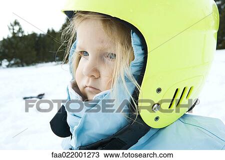 Stock Image - Toddler girl wearing winter coat and helmet, in snowy landscape, portrait. Fotosearch