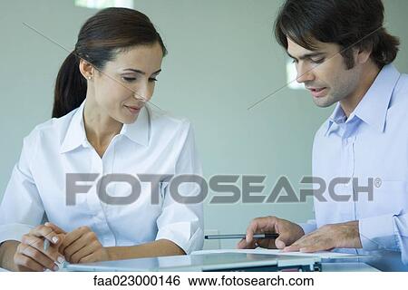 Two business associates sitting side by side, discussing document together View Large Photo Image Stock Photograph - Two business associates sitting side by side, discussing document together. Fotosearch