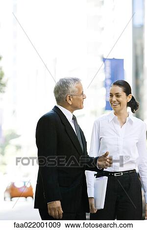 Two business associates walking together outdoors, smiling at each other, chatting View Large Photo Image Stock Photo - Two business associates walking together outdoors, smiling at each other, chatting. Fotosearch