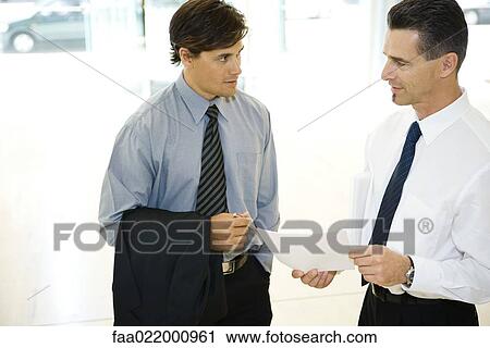 Two businessman looking at each other, discussing, one holding document View Large Photo Image Stock Image - Two businessman looking at each other, discussing, one holding document. Fotosearch