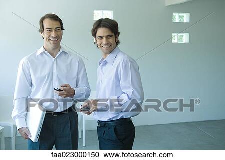 Two businessmen, each holding cell phone, looking out of frame View Large Photo Image Stock Image - Two businessmen, each holding cell phone, looking out of frame. Fotosearch