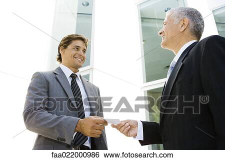 Stock Photograph - Two businessmen exchanging business card, smiling at each other, low angle view. Fotosearch