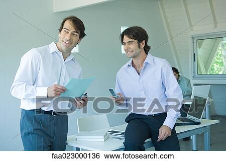 Two businessmen in office, one holding cell phone View Large Photo Image Stock Photograph - Two businessmen in office, one holding cell phone. Fotosearch