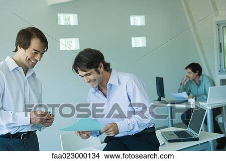 Two businessmen looking at document together in office, laughing View Large Photo Image Picture - Two businessmen looking at document together in office, laughing. Fotosearch