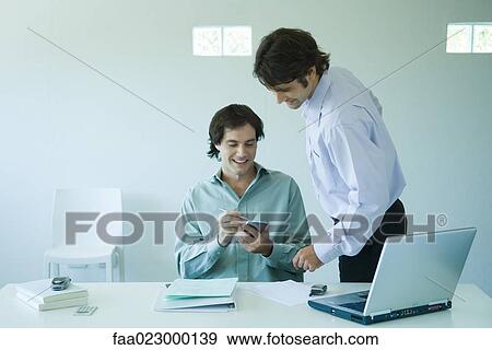 Two businessmen looking at notebook together in office View Large Photo Image Stock Photo - Two businessmen looking at notebook together in office. Fotosearch
