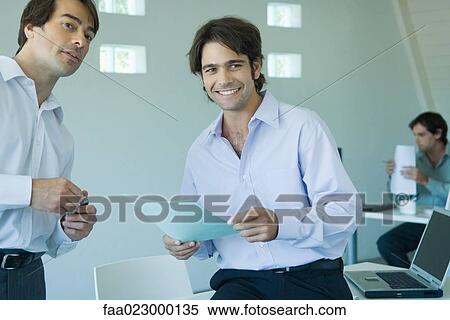 Two businessmen standing in office, looking away View Large Photo Image Stock Photography - Two businessmen standing in office, looking away. Fotosearch