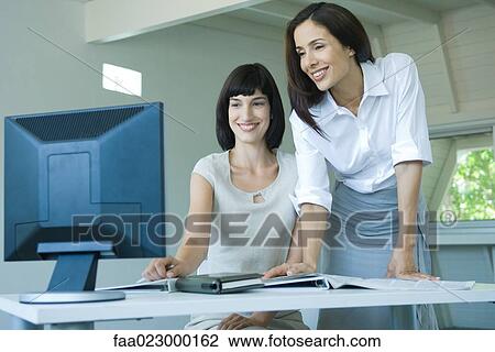Two businesswomen looking at computer monitor together, smiling View Large Photo Image Stock Image - Two businesswomen looking at computer monitor together, smiling. Fotosearch