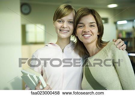 Stock Photo - Two female college students, one with arm around the other's shoulders, smiling at camera, portrait. Fotosearch