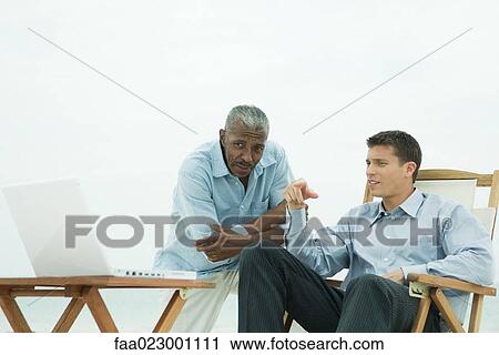 Stock Image - Two men looking at laptop together, outdoors. Fotosearch
