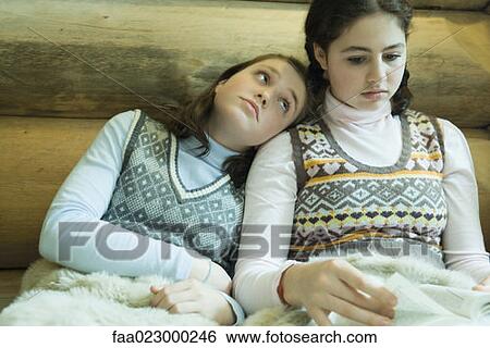 Two teen girls in winter clothes sitting under warm blanket together, one reading while other looks bored View Large Photo Image Stock Photograph - Two teen girls in winter clothes sitting under warm blanket together, one reading while other looks bored. Fotosearch