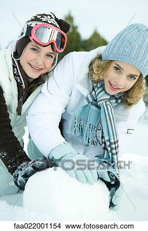 Two teenage girls crouching in snow, making snowball together, both smiling at camera View Large Photo Image Picture - Two teenage girls crouching in snow, making snowball together, both smiling at camera. Fotosearch