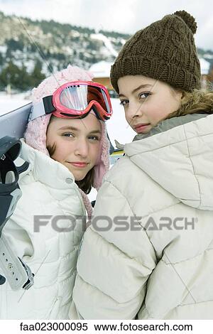 Stock Photography - Two teenage girls looking over shoulders at camera, one holding snowboard. Fotosearch