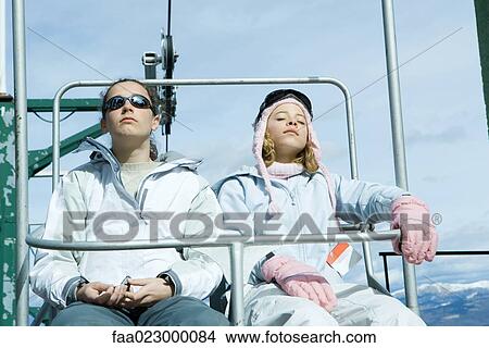 Picture - Two teenage girls riding chair lift, one's eyes closed. Fotosearch
