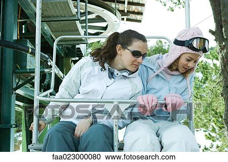 Two teenage girls sitting on chair lift, looking over side together View Large Photo Image Stock Image - Two teenage girls sitting on chair lift, looking over side together. Fotosearch