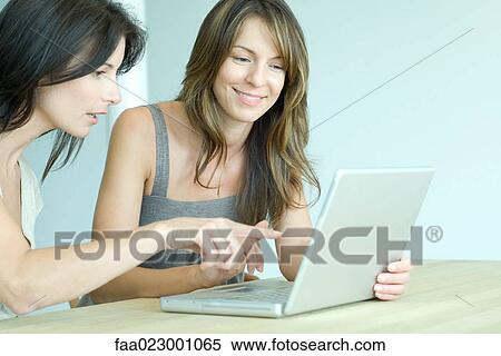 Two women sitting side by side, looking at laptop computer, one pointing View Large Photo Image Stock Photography - Two women sitting side by side, looking at laptop computer, one pointing. Fotosearch