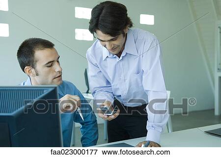 Two young businessmen looking at cell phone View Large Photo Image Stock Photo - Two young businessmen looking at cell phone. Fotosearch