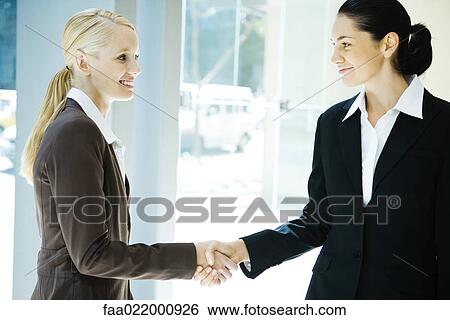 Two young businesswomen shaking hands, smiling at each other View Large Photo Image Stock Photograph - Two young businesswomen shaking hands, smiling at each other. Fotosearch