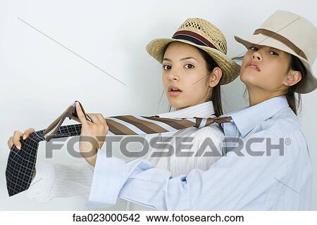 Two young female friends dressed in hats and ties, one behind the other, looking at camera View Large Photo Image Stock Image - Two young female friends dressed in hats and ties, one behind the other, looking at camera. Fotosearch
