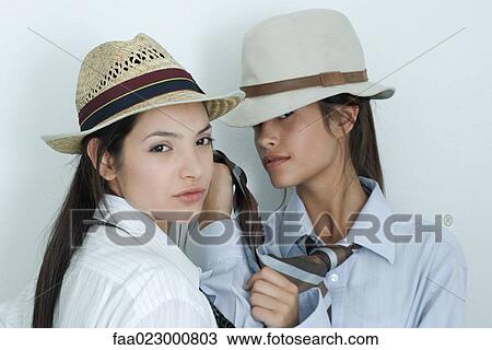 Two young female friends dressed in button down shirts, ties and hats, one holding the other's tie, looking at camera, portrait View Large Photo Image Stock Image - Two young female friends dressed in button down shirts, ties and hats, one holding the other's tie, looking at camera, portrait. Fotosearch