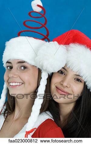 Stock Image - Two young female friends dressed in Christmas costumes, smiling at camera, portrait. Fotosearch