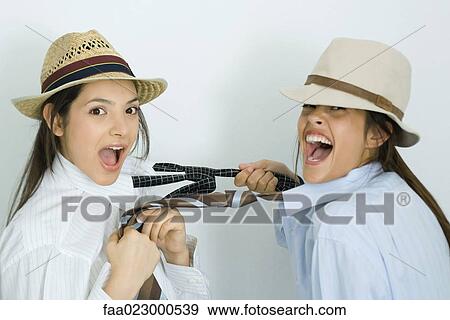 Two young female friends dressed in hats, pulling each other's ties, laughing at camera View Large Photo Image Stock Photo - Two young female friends dressed in hats, pulling each other's ties, laughing at camera. Fotosearch