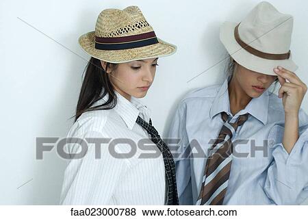 Stock Photo - Two young female friends dressed in button down shirts, ties and hats, looking down, portrait. Fotosearch