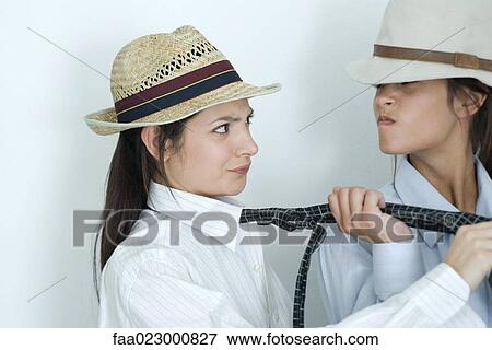 Stock Photo - Two young female friends dressed in button down shirts, ties and hats, one pulling on the other's tie. Fotosearch