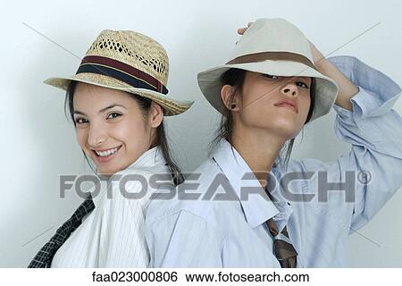 Stock Photograph - Two young female friends dressed in button down shirts, ties and hats, looking at camera, portrait. Fotosearch