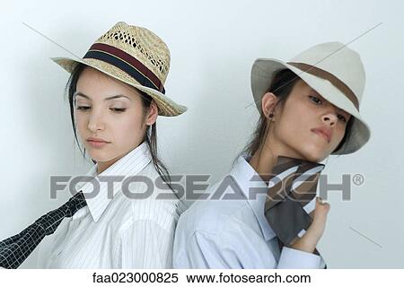 Two young female friends dressed in button down shirts, ties and hats, standing back to back, portrait View Large Photo Image Stock Photography - Two young female friends dressed in button down shirts, ties and hats, standing back to back, portrait. Fotosearch