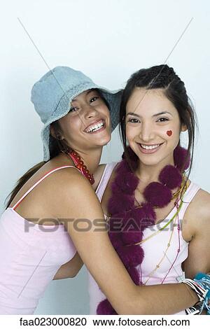 Stock Image - Two young female friends embracing, smiling at camera, portrait. Fotosearch