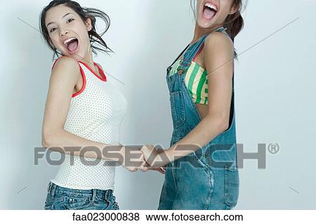 Two young female friends holding hands and jumping for joy, smiling at camera, portrait View Large Photo Image Stock Photo - Two young female friends holding hands and jumping for joy, smiling at camera, portrait. Fotosearch