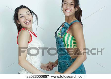 Two young female friends holding hands and jumping for joy, smiling at camera, portrait View Large Photo Image Stock Photo - Two young female friends holding hands and jumping for joy, smiling at camera, portrait. Fotosearch