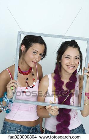 Two young female friends holding up picture frame, smiling at camera, portrait View Large Photo Image Picture - Two young female friends holding up picture frame, smiling at camera, portrait. Fotosearch