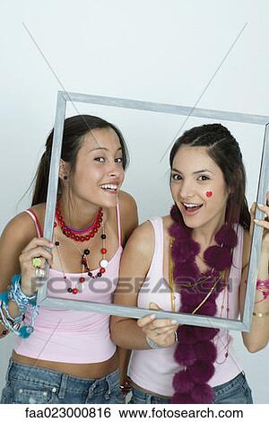 Two young female friends holding up picture frame, smiling at camera, portrait View Large Photo Image Stock Photograph - Two young female friends holding up picture frame, smiling at camera, portrait. Fotosearch